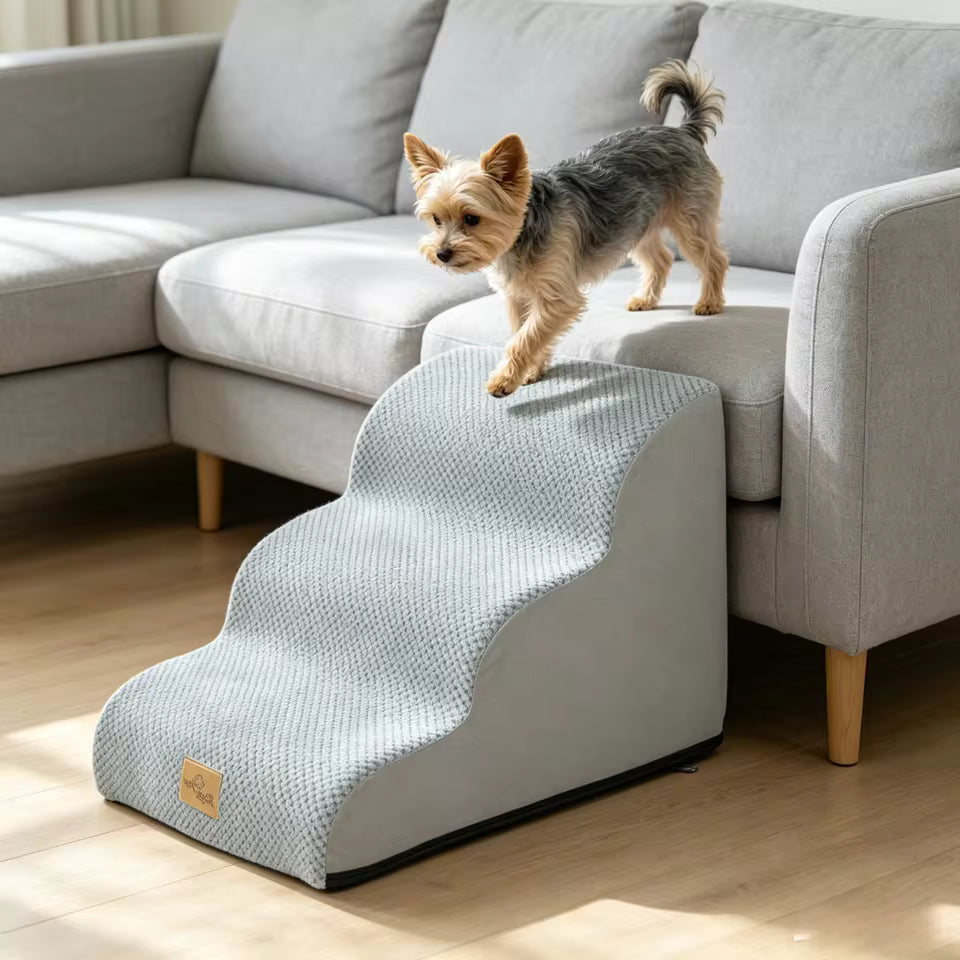 A small Yorkshire Terrier climbs up curved gray foam pet stairs leading to a gray sofa.