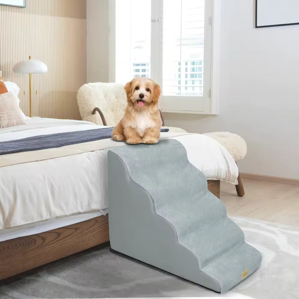 A small fluffy dog sits atop curved gray pet stairs next to a bed.