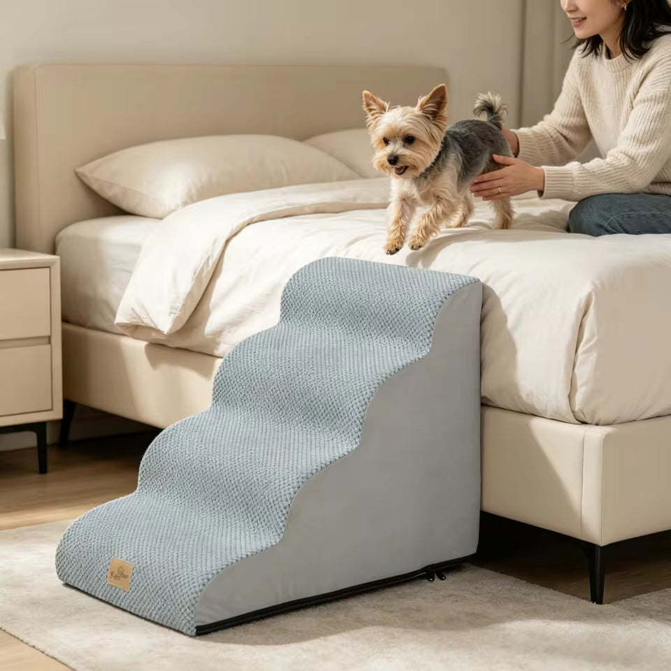 A small dog jumps off a bed next to gray pet stairs with a woman nearby.