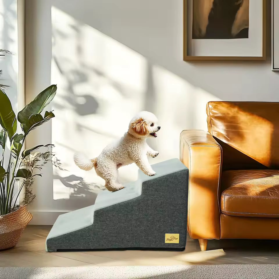 A small dog climbing a grey 4-step pet staircase beside a brown leather couch.