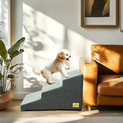 A small dog climbing a grey 4-step pet staircase beside a brown leather couch.
