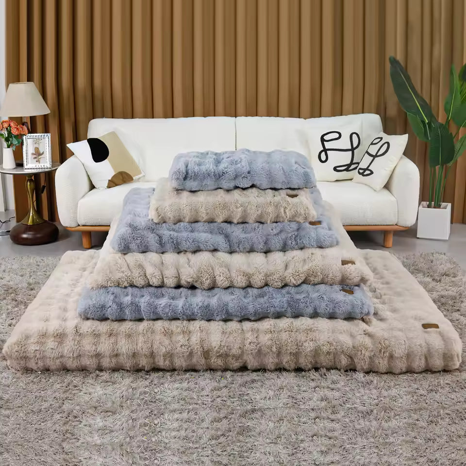 A stack of plush, faux fur dog beds in alternating gray and beige colors in front of a white sofa.