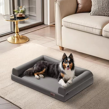 A fluffy tricolor dog relaxing on a grey orthopedic bolster bed inside a bright living room.