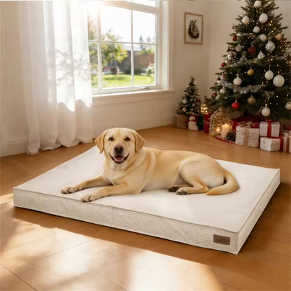 A smiling yellow labrador lies on a light-colored rectangular dog bed near a decorated Christmas tree.