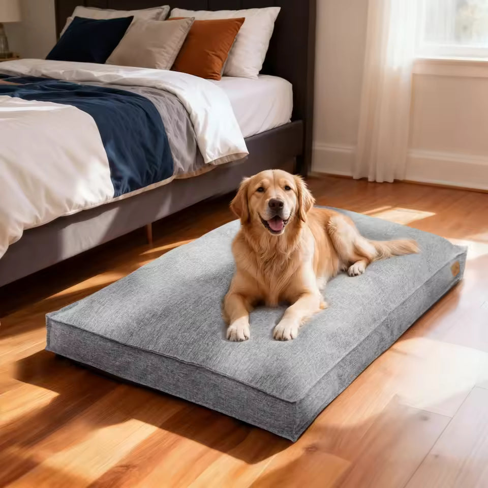 A golden retriever rests on a gray dog bed near a bed in a bedroom.