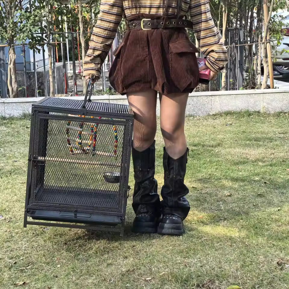 A person holding a large metal bird cage outdoors on grass.