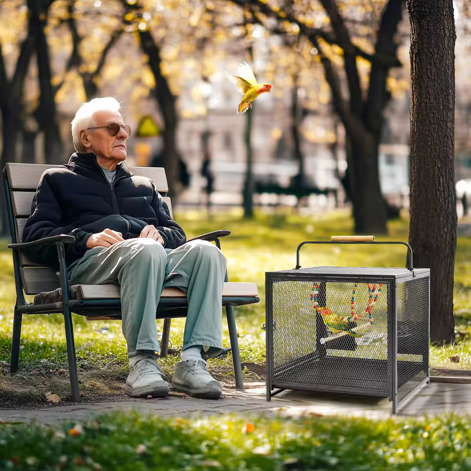 An elderly man sitting on a park bench next to a bird cage with a bird flying nearby.