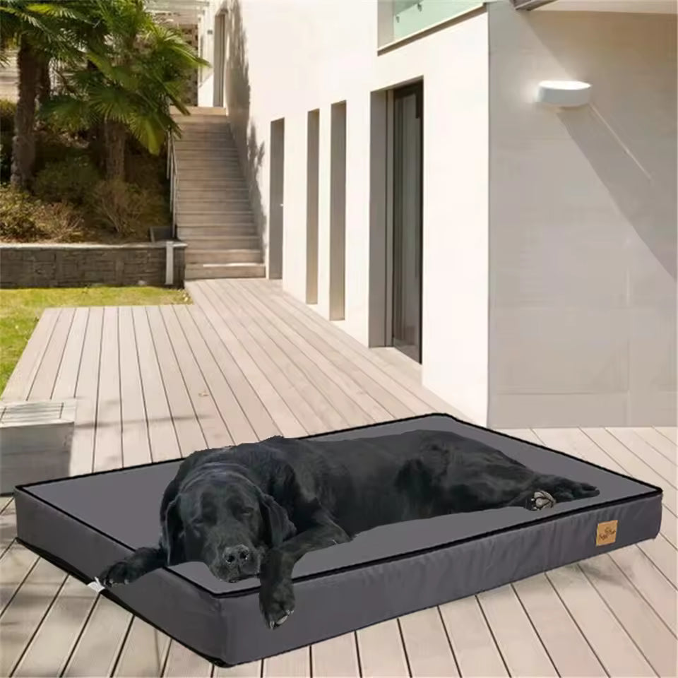 A black dog sleeping comfortably on a large grey orthopaedic pet bed outdoors.