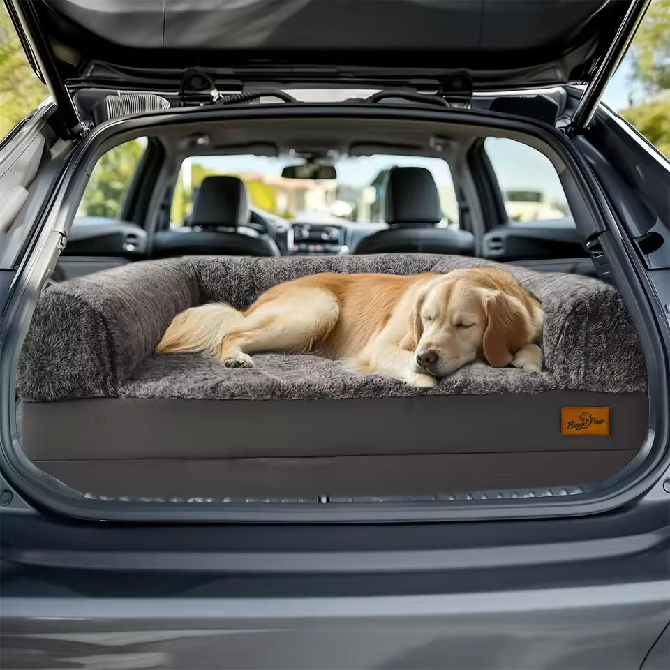 A golden retriever sleeping on a gray pet bed inside the trunk of a car.