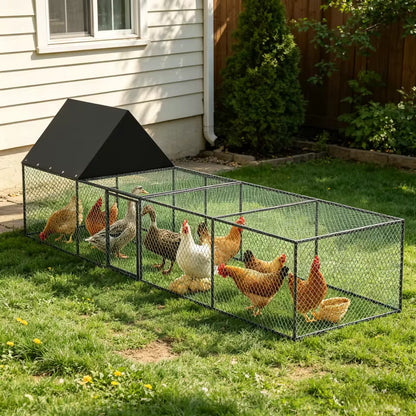 A long metal wire chicken coop with a black roof and a group of chickens and ducks inside on a lawn.
