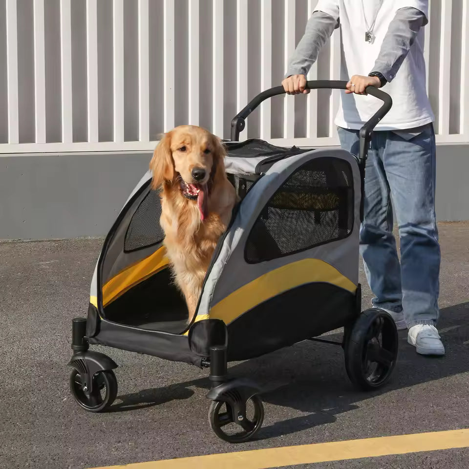 Golden Retriever riding in a gray and yellow pet stroller pushed outdoors by a person.