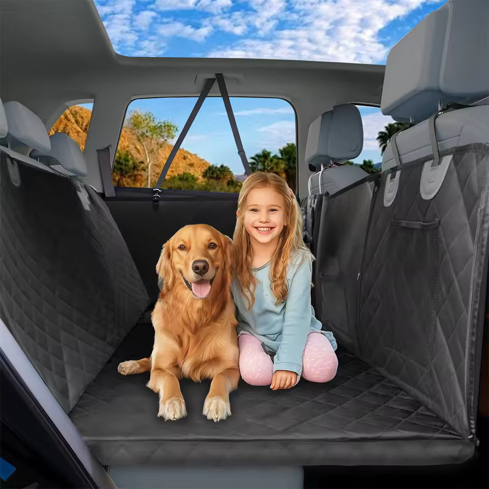 A young girl and a golden retriever sit together on a black quilted pet seat cover in a car's back seat.